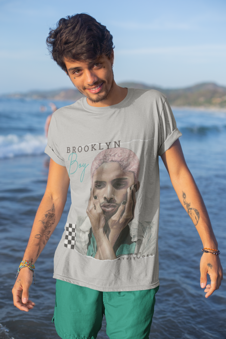 Man with tattoos in front of the sea wearing a grey t-shirt and green pants