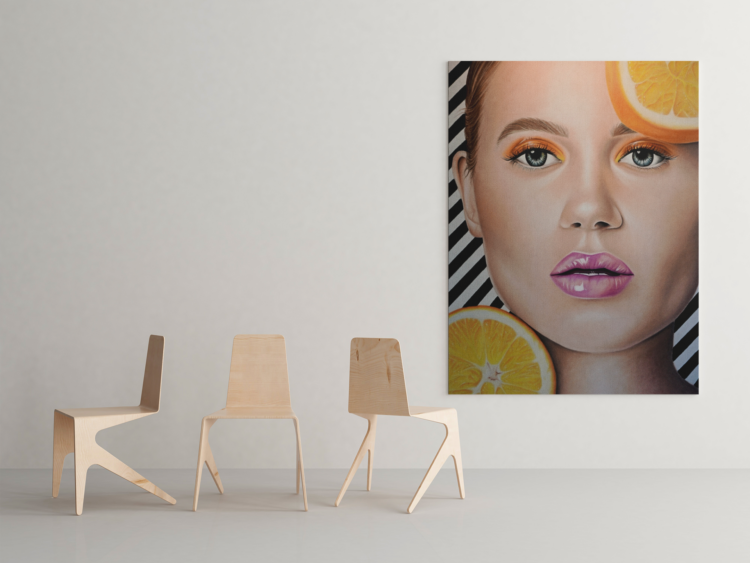 Big pastel drawing of a woman with purple lips and orange eye shadow and an orange in top right coner and left bottom coner with a black and whit striped bagground hanging on a wall next to three wooden chairs