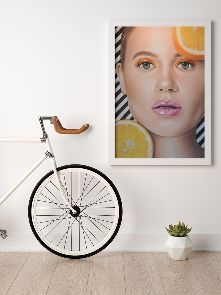 Big pastel drawing of a woman with purple lips and orange eye shadow and an orange in top right coner and left bottom coner with a black and whit striped bagground in a white frame hanging on the wall next to a white bicycle