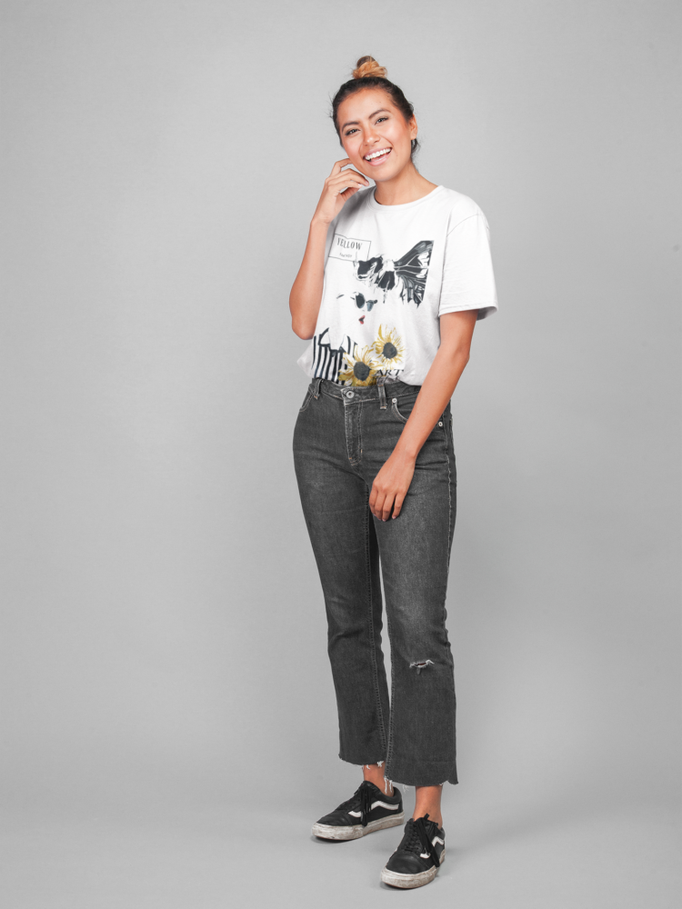 Smiling woman wearing black jeans and White t-shirt with a motive of a woman in a black and a white shirt with two sunflowers in the right coner and a skull butterfly next to her head
